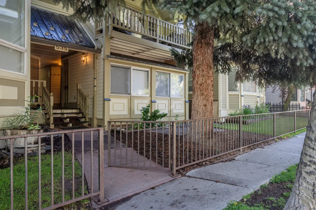 The image captures the welcoming entrance steps of the condo, featuring a decorative railing, a large tree, and a cozy balcony. The scene suggests easy walkability and access, echoing the family-friendly and approachable vibe of the neighborhood.