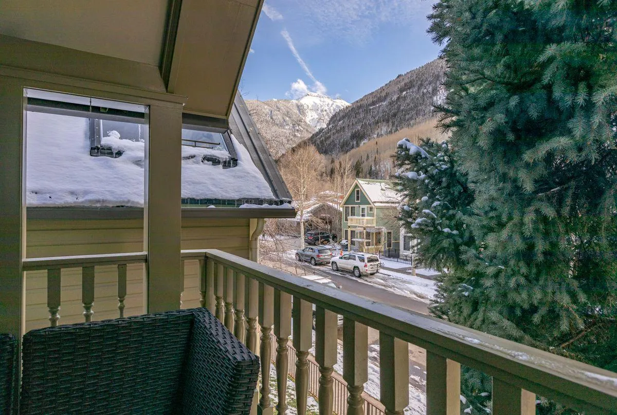 A peaceful exterior view from a private balcony showcases snow-covered rooftops, evergreen trees, and awe-inspiring mountain vistas. The serene setting invites moments of relaxation after outdoor adventures, all within sight of Telluride’s natural beauty.