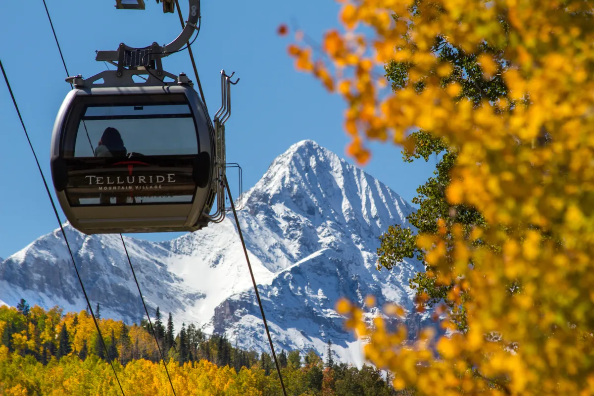 This image features the iconic Telluride gondola set against a backdrop of snow-capped mountains and vibrant autumn foliage. The gondola, visible in motion, hints at easy access to mountain adventures and panoramic views, while the surrounding scenery captures the adventurous spirit of Telluride.