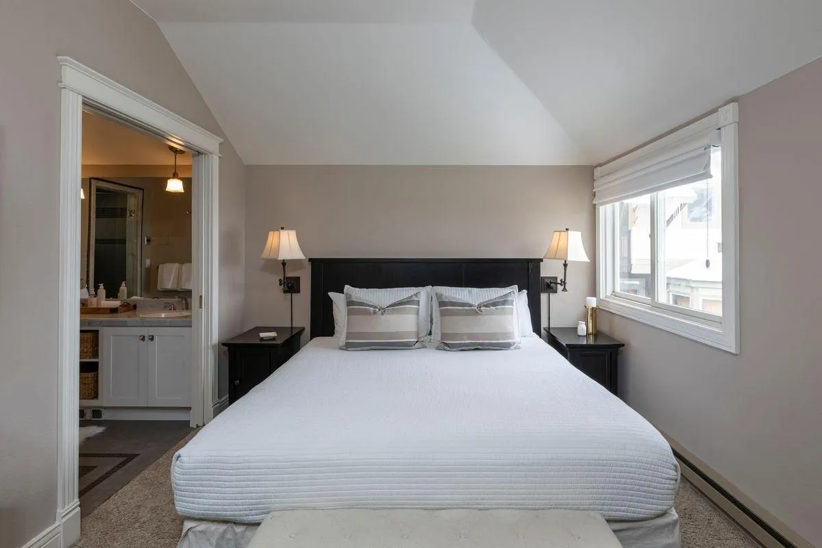 A tranquil bedroom featuring a plush bed, nightstands with lamps, and a window streaming in natural light. The room feels peaceful and restful, ideal for relaxing after a day out.