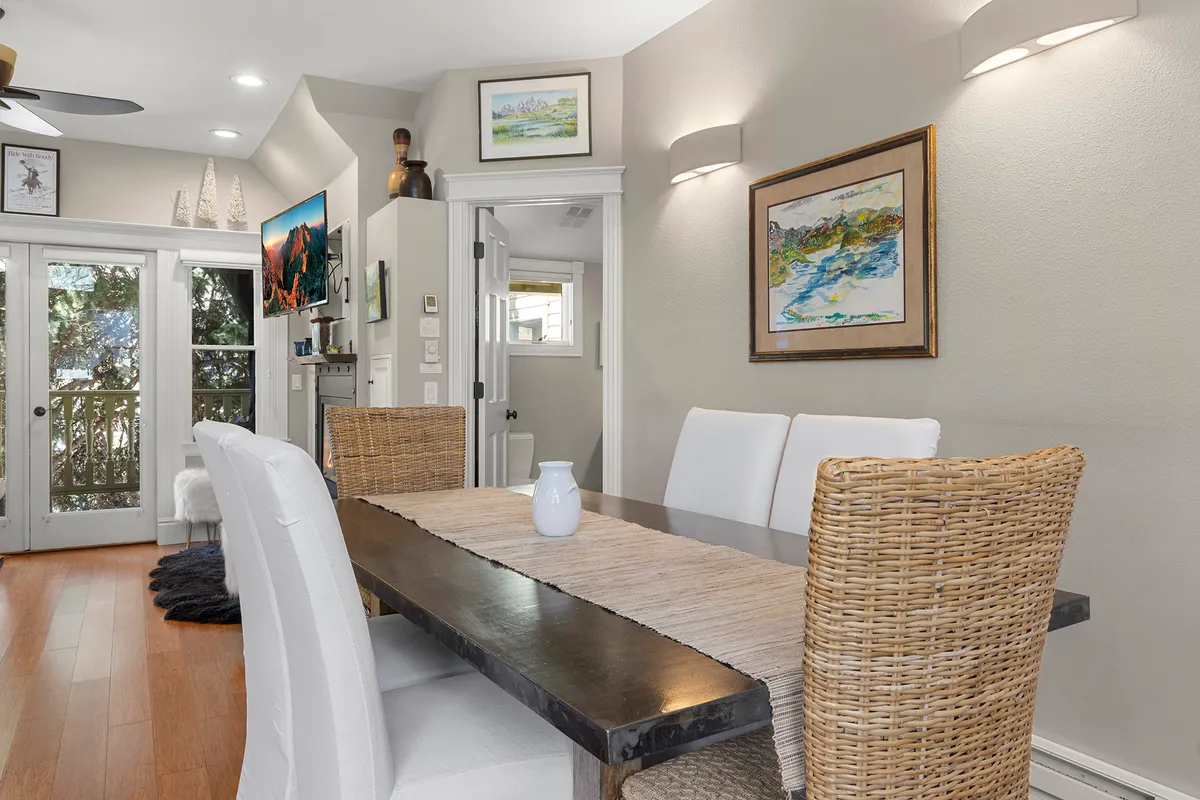 A sunlit dining area with a large table, artwork on the walls, and abundant natural light streaming through the windows. The setup invites family meals and gatherings, reinforcing the home's suitability for families traveling with children.