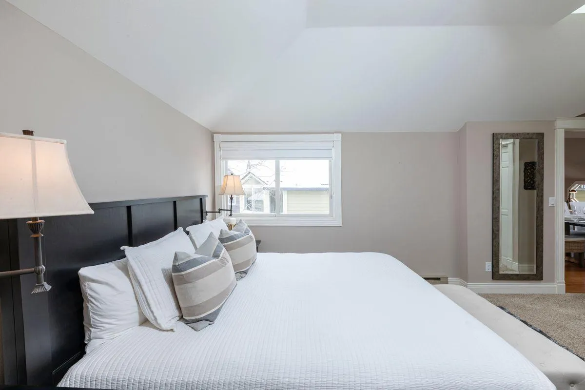 A tranquil bedroom scene featuring a comfortable bed with decorative pillows, bedside lamps casting soft light, and a window that allows natural light to spill into the space, inviting relaxation and quiet moments.