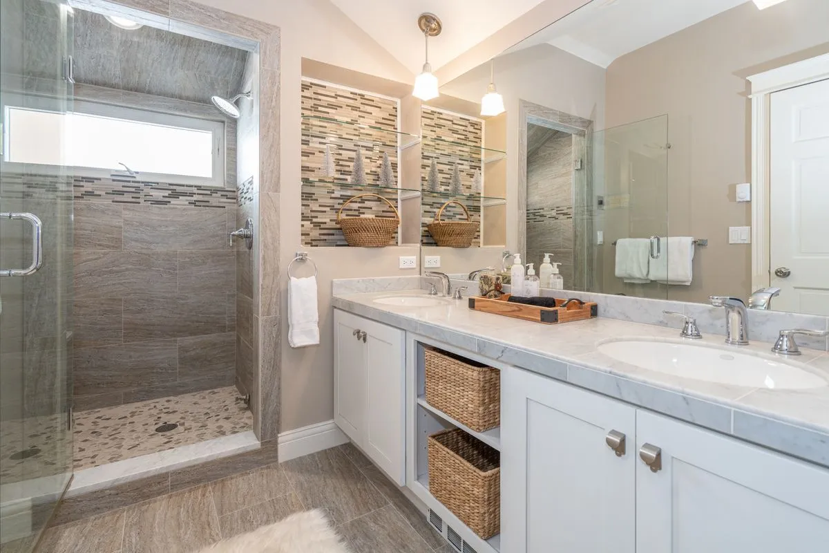 A stylish en-suite bathroom with a double vanity, glass shower enclosure, and textured wall tiles. The space is organized and bright, suggesting a luxurious spot for morning or evening routines.